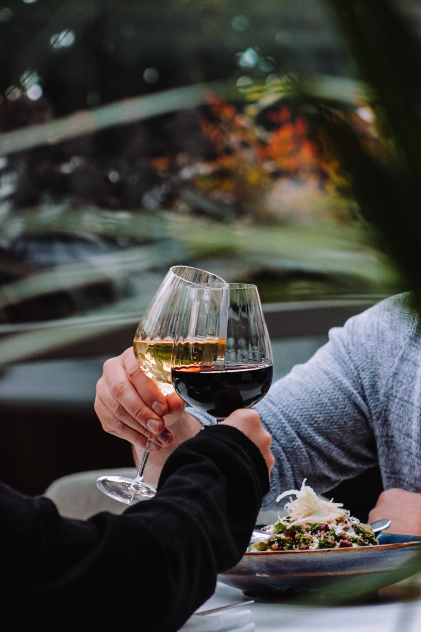 A close-up shot of a hand holding a glass of red wine during a tasting, with a meal blurred in the background.