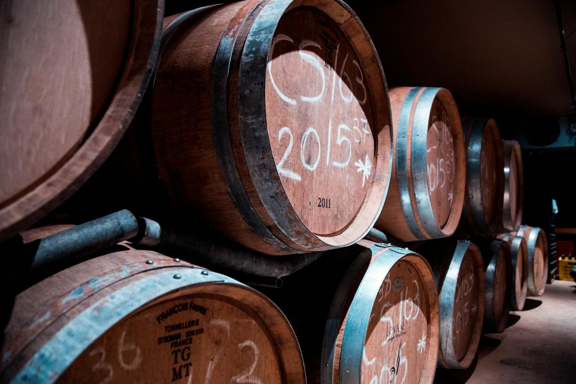 Rows of oak barrels in a dimly lit wine cellar, symbolizing the aging process of Rioja Reserva
